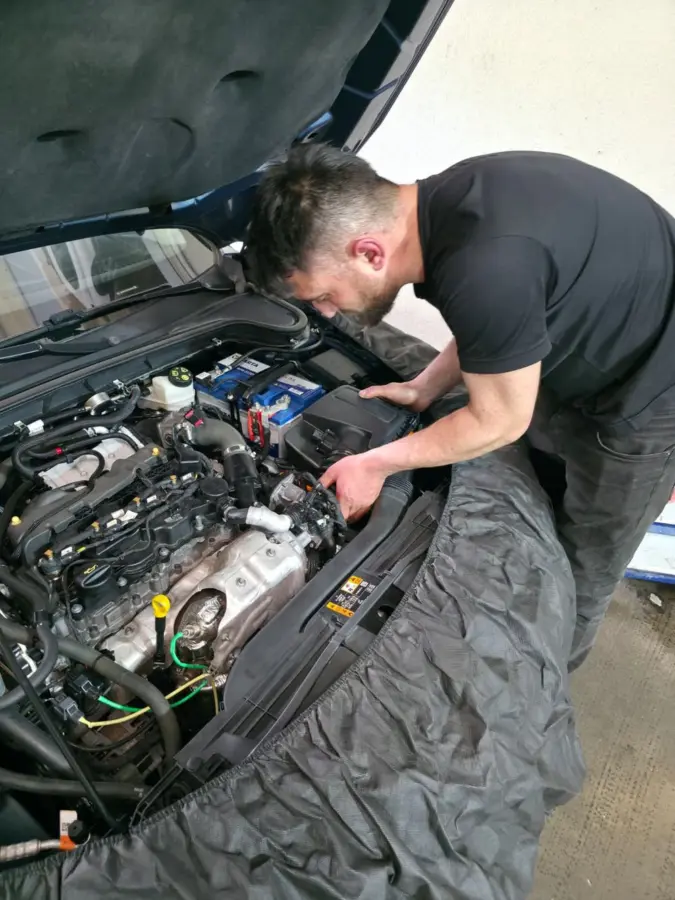 Usta, korumalı çamurlukla açık kaputlu aracın motor bölmesinde çalışıyor